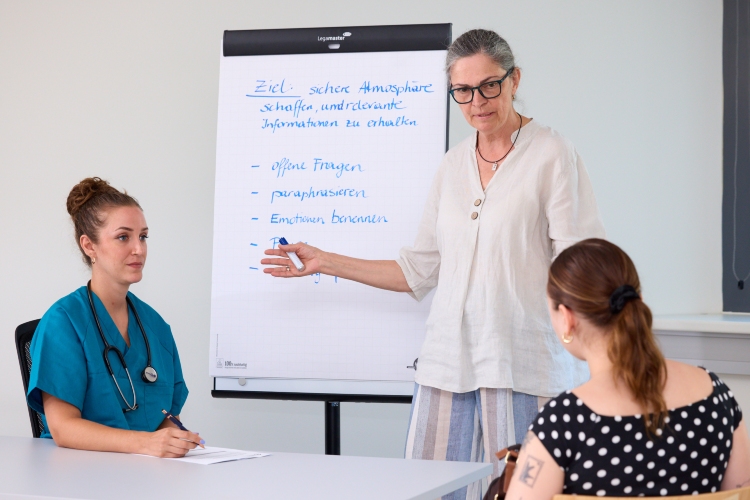 © HCW/Schedl Eine Lehrperson erläutert Inhalte an einem Flipchart, während zwei Teilnehmende die Ausführungen verfolgen.