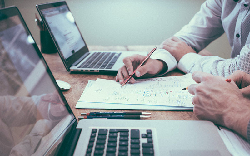 zwei Personen am Arbeitsplatz mit Notebooks und Notizen