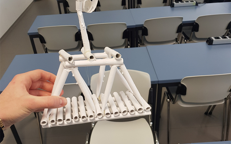 In einer Hand eine aus Papier gebaute Brücke