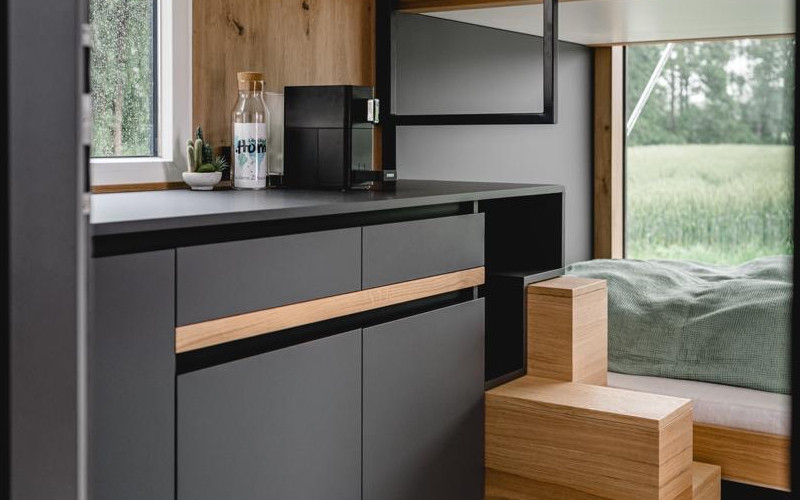 Innenbereich vom LibertydotHome Tiny House mit Küchenzeile in Grau und einem Bett vor einem großen Fenster