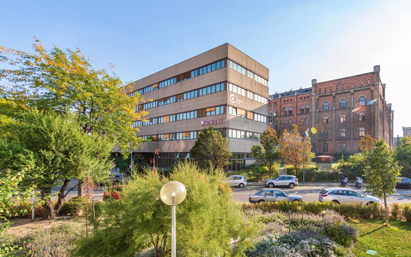 Neuer Studienstandort Kelsenstraße, Grünflachen im Vordergrund, danach Autos und Studienstandort, dahinter Arsenalgebäude