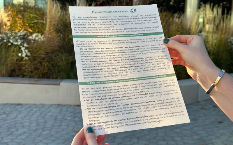 © HCW Zwei Hände halten ein DIN-A4-Blatt mit der Überschrift „Planetary Health Charta 2030“.