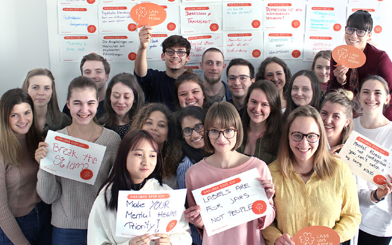 Studierende und Lehrende mit Plakaten vor einer Wand mit Statements