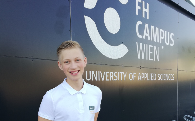 Ferialpraktikant Paul Klein vor dem Gebäude der Hochschule Campus Wien und dem Logo 