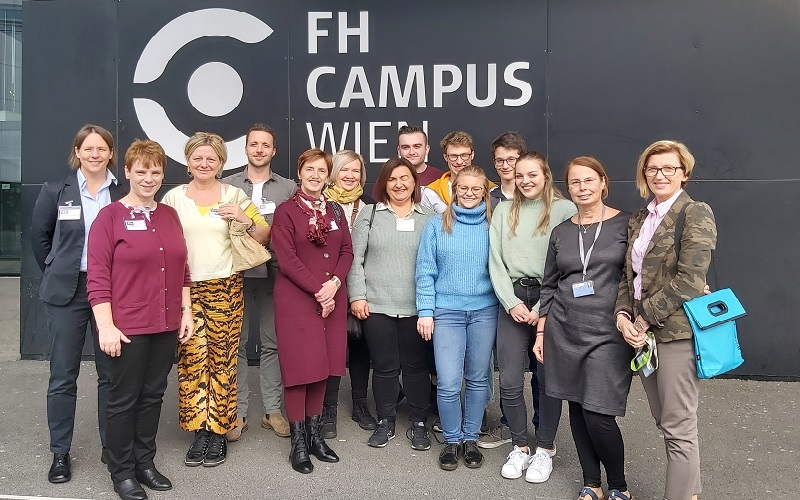 Frauen und Männer vor dem Gebäude und vor dem Logo der Hochschule Campus Wien, 
