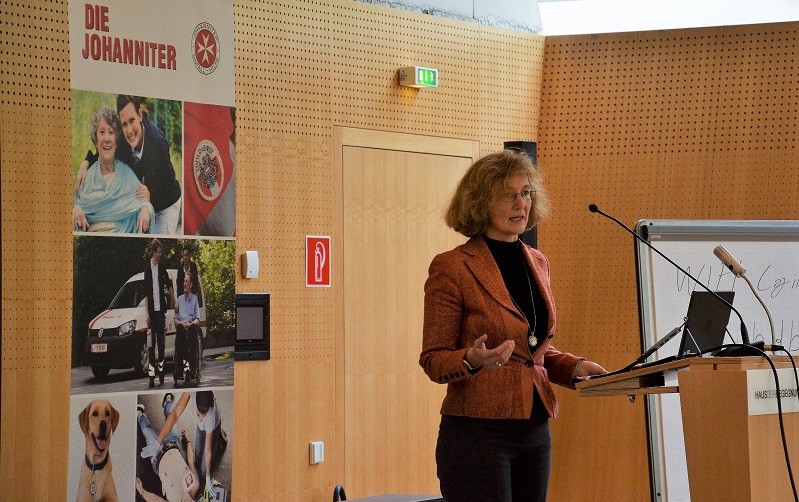 Vortragende elisabeth Haslinger-Baumann am Podium, dahinter ein Rollup von den JOhannitern