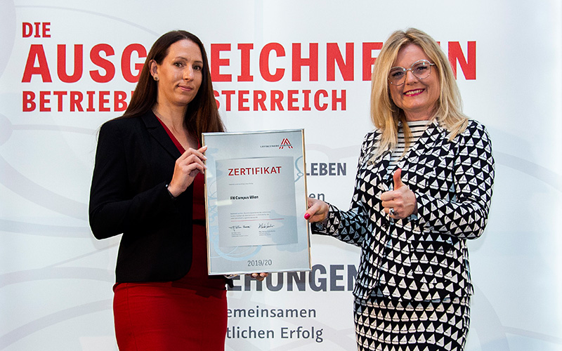 Zwei Frauen stehen vor einem Roll-up auf dem "Die ausgezeichneten Betriebe in Österreich" steht. Links steht Daniela Janko, Qualitätsleitung der Hochschule Campus Wien, rechts steht Monica Rintersbacher, Geschäftsführerin Leitbetriebe Austria