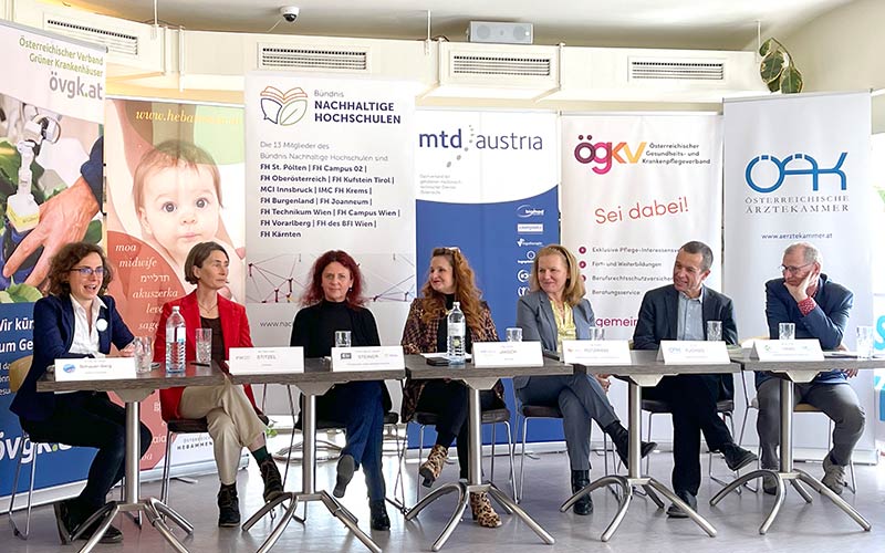 Sieben Personen sitzen auf einem Podium