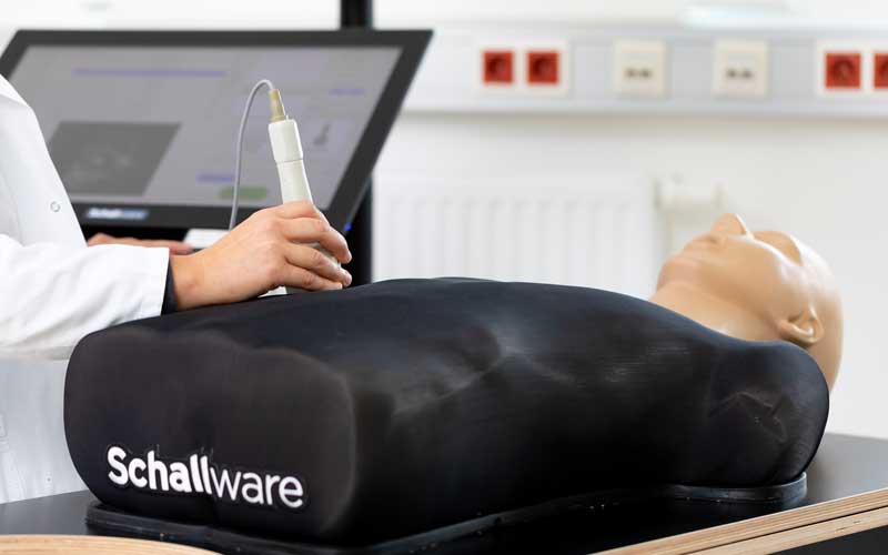 Lehrende lenkt die Ultraschallsonde über einen Patient*innen-Dummy