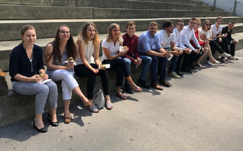 Männer und Frauen auf einer Stufe sitzend und eine Jause essend.