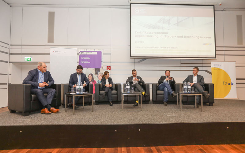 Personen sitzen auf Sessel auf der Bühne und diskutieren