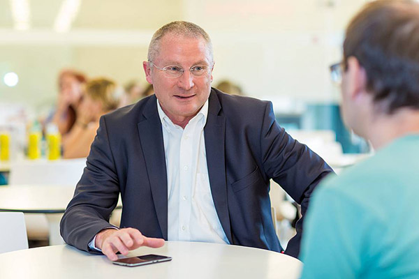 Herr mit Brille in weißem Hemd und schwarzem Sacko im Gespräch in der Cafeteria der F H Campus Wien
