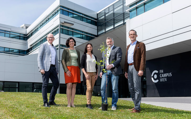 Das Team steht mit dem Baum vor dem FH-Gebäude am Hauptstandort in Favoriten