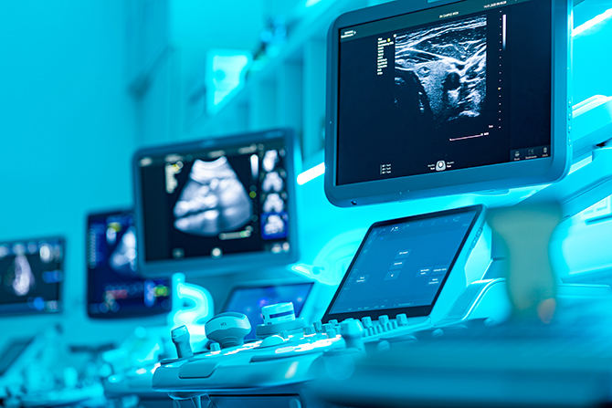 Ein blau ausgeleuchteter Raum mit Monitore auf denen Ultraschallbildern zu sehen sind.