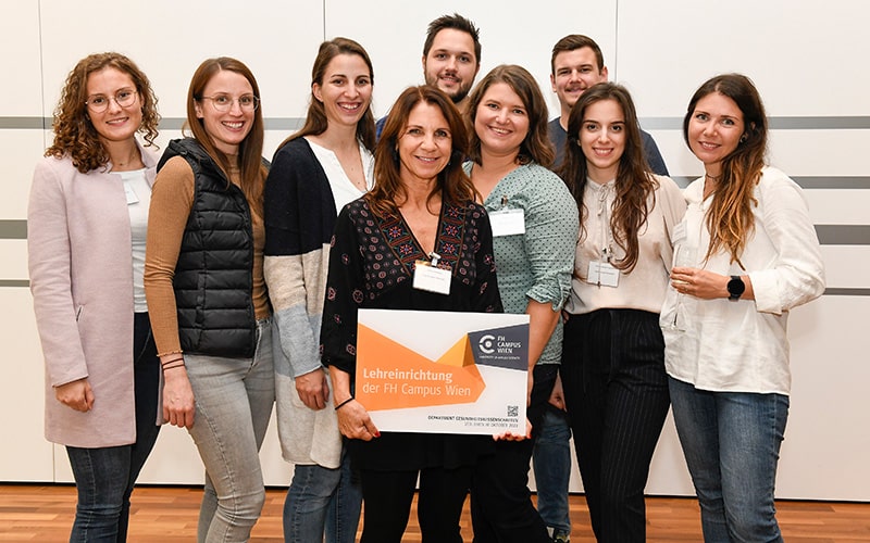 Gruppenfoto mit neun Personen und eine Dame in der Mitte hält eine Lehreinrichtungstafel
