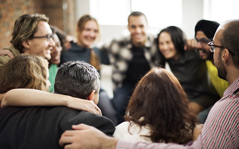 Eine Gruppe von Personen steht in einem Kreis und hält sich an den Schultern