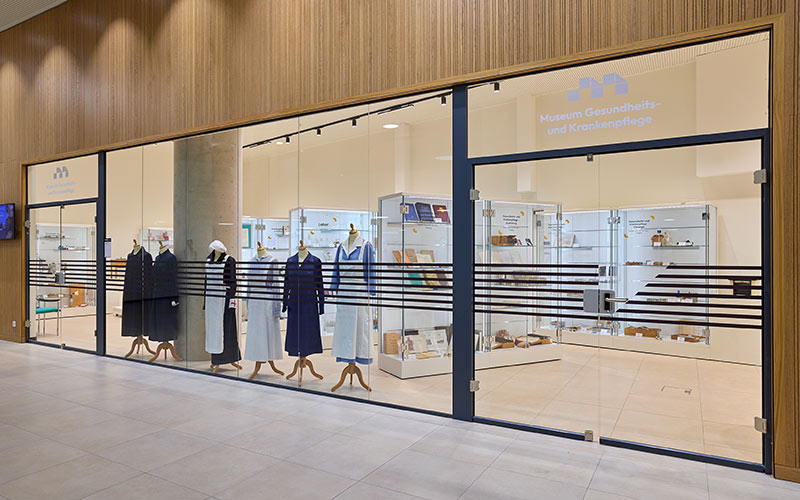Große Schaufenster und Eingang zum Museum im Gebäude der Hochschule Campus Wien. Vitrinen und unterschiedliche Dienstkleidungen aus der Krankenpflege