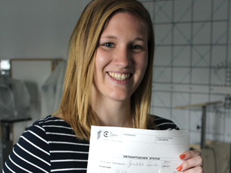 Studierende lächelt in die Kamera und hält ein Blattpapier mit Daten in die Höhe.