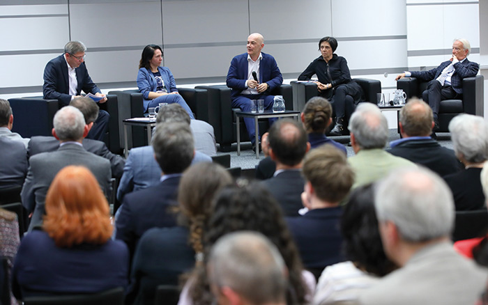 © Schedl / FH Campus Wien Menschen schauen zu während eine Diskussion auf einem Podium geführt wird