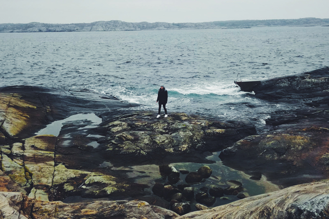 Frau steht auf großem Stein an einer Küste