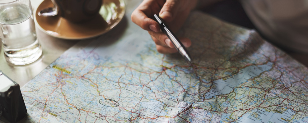 Weltkarte verteilt auf einem Tisch, einer Kaffeetasse und einer Hand, die einen Stift hält