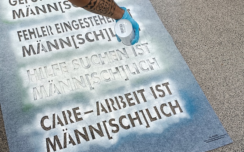 Verschiedene Slogans mit "Männ[sch]lich werden auf den Boden gesprayt
