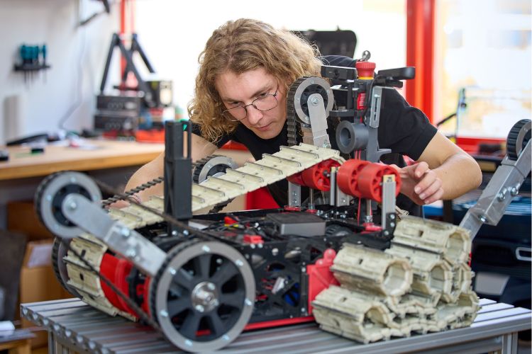 Ein Student schraubt an einem selbstgebauten Roboter