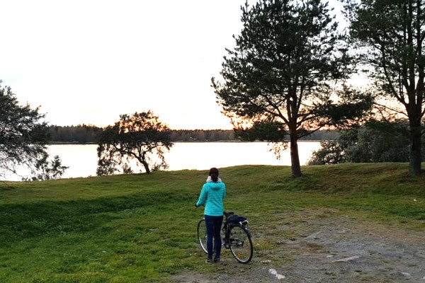 Frau in türkiser Jacke steht mit Fahrrad vor Gewässer