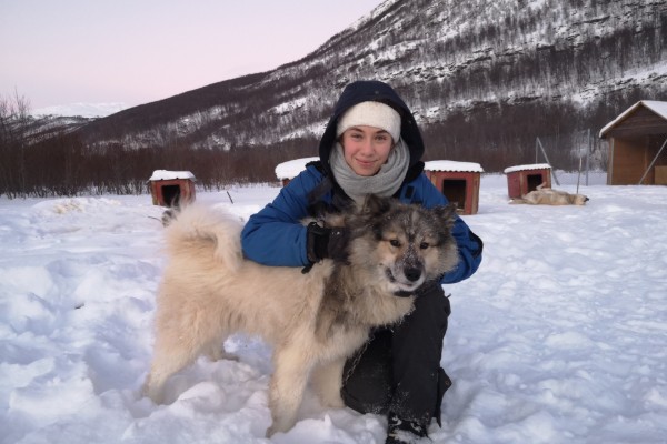 Junge Frau in Winterkleidung umarmt Hund im Schnee