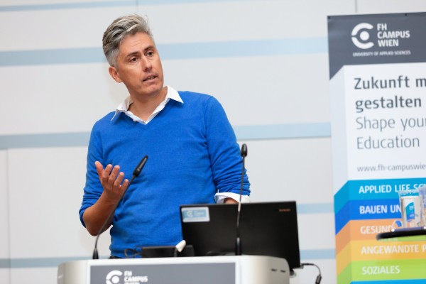 Herr in blauem Pullover am Rednerpult