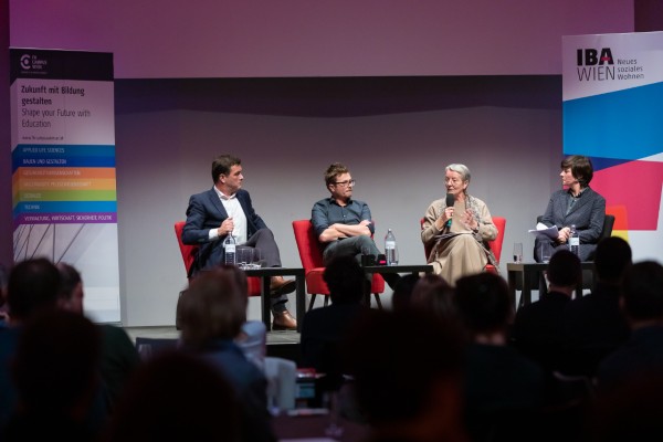 Vier Personen auf roten Sesseln vor Publikum