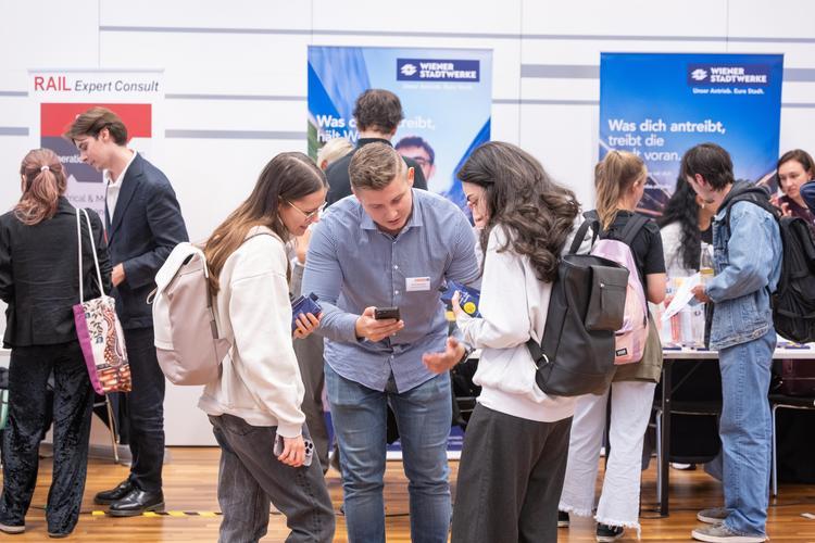 Zwei Besucher*innen der Karrieremesse Technik tauschen mit Mitarbeiter eines Unternehmens Kontaktdaten aus