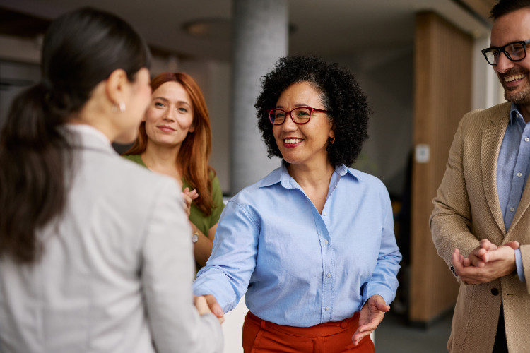 © Igor Suka/istock.com Zwei Frauen geben sich die Hand, eine Frau und ein Mann stehen im Hintergrund