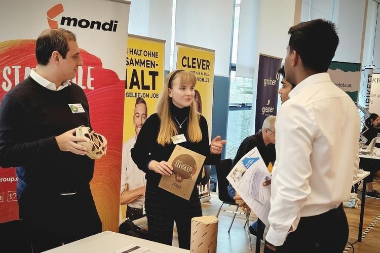 Studierende stehen vor Ausstellerstand und informieren sich