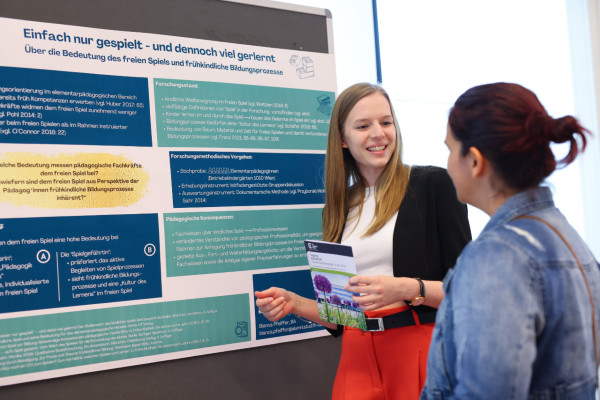 Eine Studierende steht vor ihrem Poster und erklärt es einer Teilnehmerin