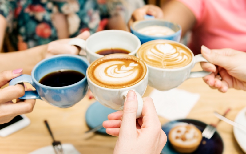 Fünf Tassen mit Kaffee, mit denen angeprostet wird