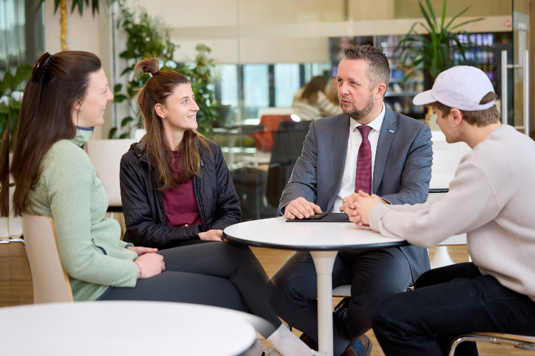 © Hochschule Campus Wien/Schedl Rektor Heimo Sandtner sitzt mit Studierenden am Tisch.
