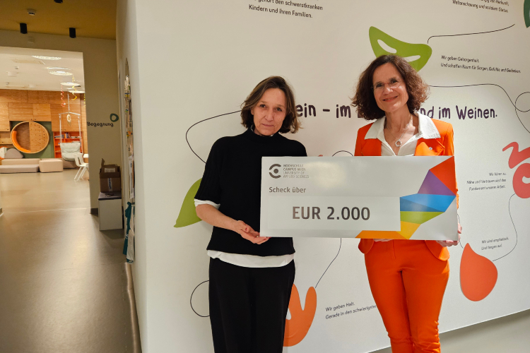 Doris Link (Hochschule Campus Wien) und Katharina Beitl (MOMO Kinderpalliativzentrum) posieren mit einem Scheck über 2.000 Euro. 