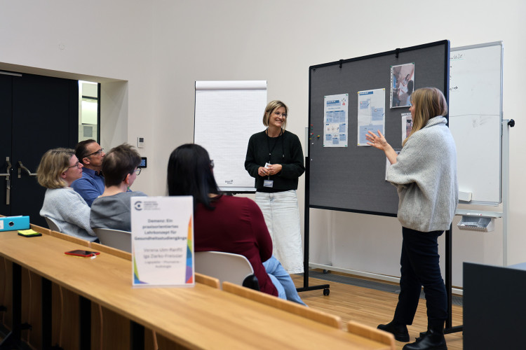 Eine Gruppe von Leuten diskutiert vor einer Pinnwand, auf der Dokumente hängen. 
