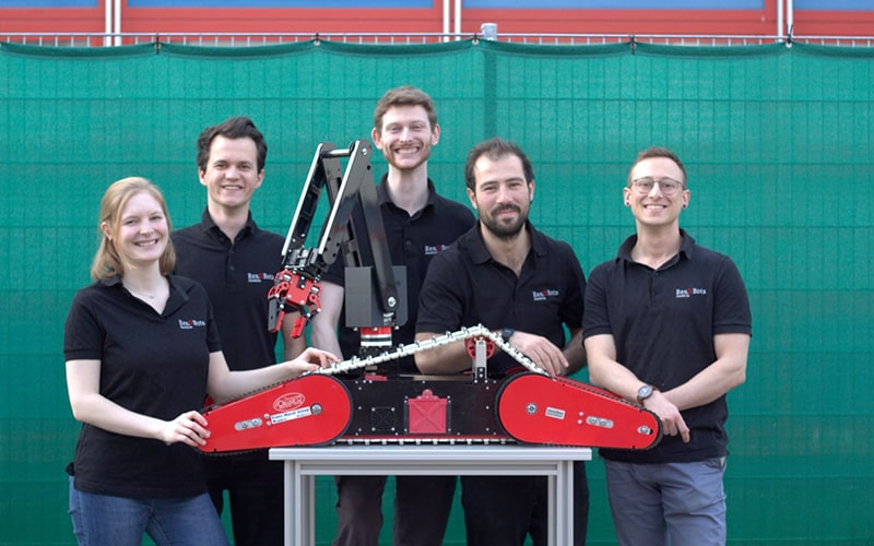 Eine Gruppe von Menschen, vier Männer und eine Frau, steht hinter einem Roboter.