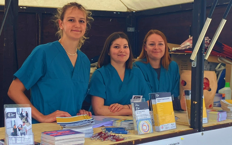 Drei Personen mit Foldern in einem Informationsstand