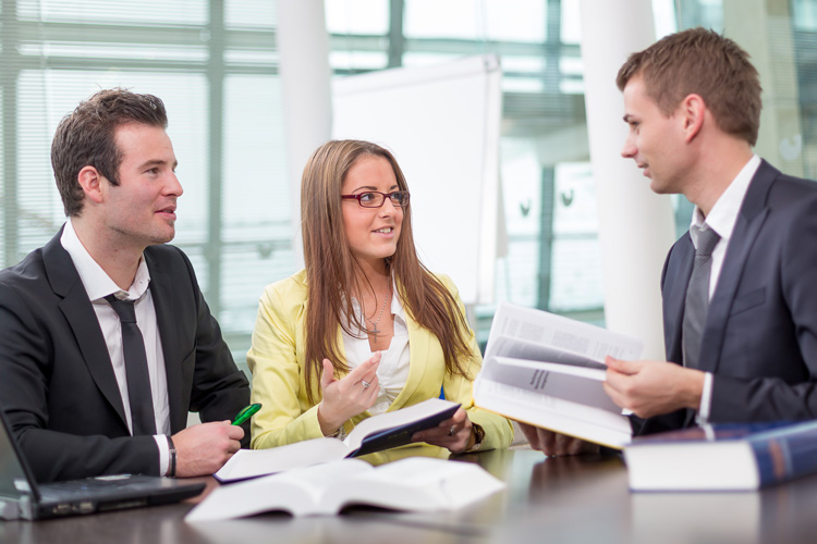 Drei Menschen, ein Mann, eine Frau und ein Mann sitzen gemeinsam am Tisch und sprechen miteinander.