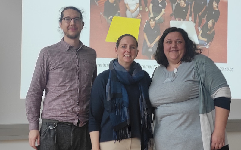 Drei PErsonen vor einer Leinwand in einem Hörsaal