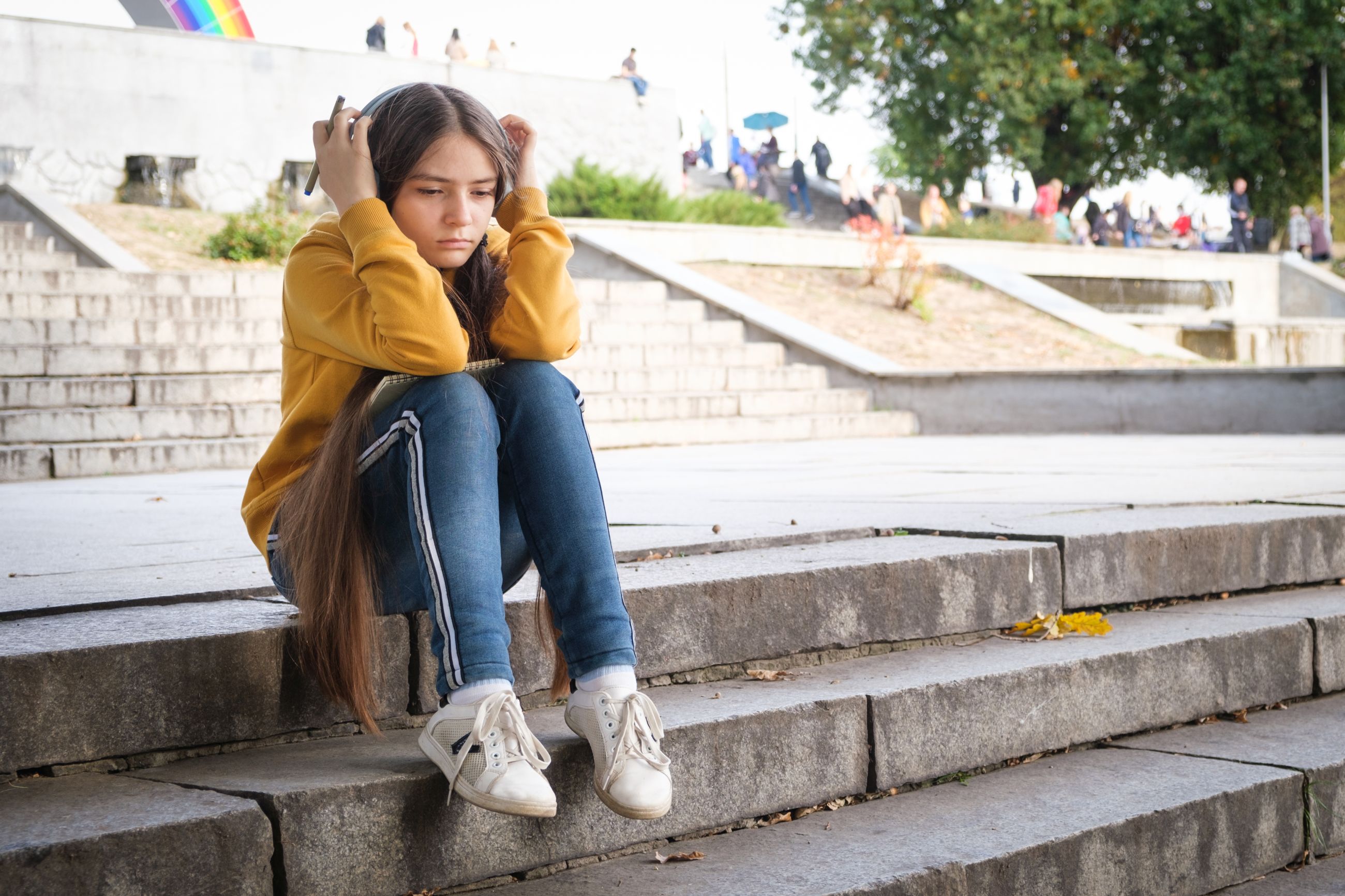 A sad teenager sitting on a public staircase, covering her/is head with the hands.