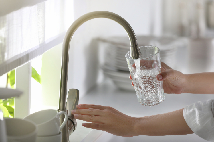 Eine Frau füllt ein Glas mit Wasser unter dem Wasserhahn. 